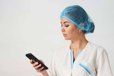 Portrait of female doctor using her mobile phone on white background with copy space. Young nurse...