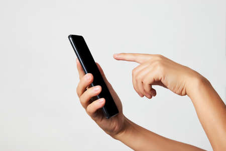 Woman holding smartphone with black screen. Woman hand holding phone on white background with copy space. Hand with blank cellphone display, close-upの写真素材