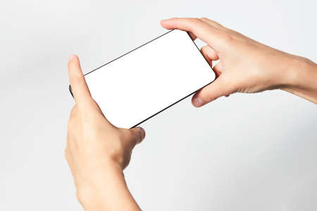 Woman hand holding phone on white background with copy space. Woman holding smartphone with white screen. Hand with blank cellphone display, close-upの写真素材