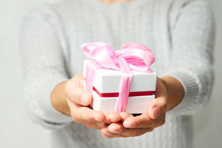 Female hands holding small gift box with ribbon on white background. Christmas, New Year,...