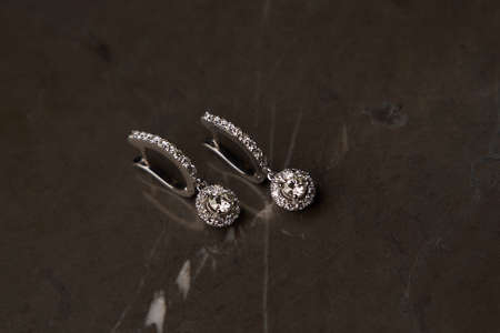Diamond earrings with gemstones on a grey marble background. Trendy diamond earring, close-up, selective focus. Luxury female jewelryの写真素材