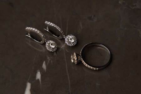 Diamond earrings and ring on a grey marble background. Trendy diamond ring with earring, close-up, selective focus. Luxury female jewelryの写真素材
