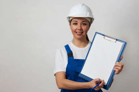 Portrait of young woman worker standing on white background with copy space. Female worker wearing workwear uniform and protective hard hatの写真素材