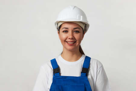 Portrait of young woman worker standing on white background with copy space. Female worker wearing workwear uniform and protective hard hatの写真素材