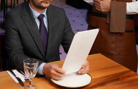 Man with menu in a restaurant taking order at table, close-up. Waiter taking the order from a businessman in restaurantの写真素材