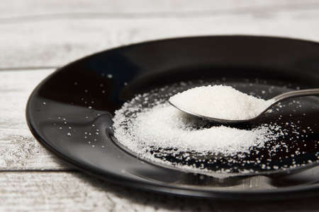 Teaspoon with sugar on a black plate.  Small spoon with granulated sugar close-up. Diabetes concept.