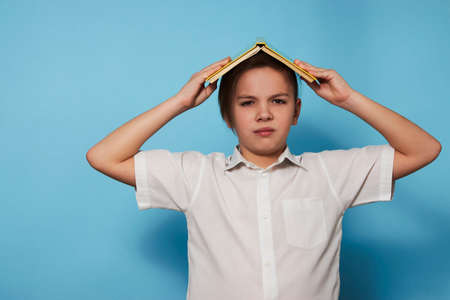 Portrait school boy with a book over blue background with copy space. Ten years old child with book, close-up. Education conceptの写真素材