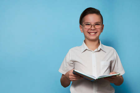 Portrait school boy with a book over blue background with copy space. Ten years old child with book,...