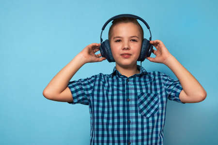 Boy listening music with headphones over blue background. Teenager boy in blue shirt wearing...