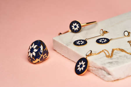 Women's jewelry on pink background. Golden jewellery set with earrings, bracelet and necklace with...