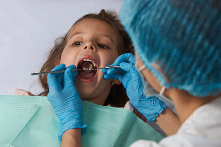 Girl visiting dentist. Little girl with open mouth sitting in the dentist's chair, close-upの写真素材