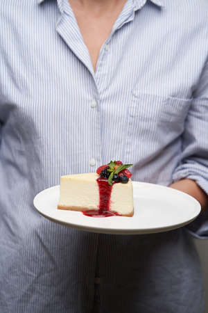 Woman with a piece of cheesecake, close-up. Hand holding cheesecake with berriesの写真素材