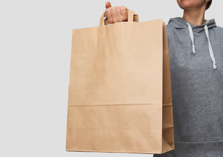 Woman holding brown paper bag on white background with copy space. Delivery and shipping service concept. Hand with paper shopping bag, close-up.の写真素材