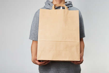 Woman holding brown paper bag on white background with copy space. Delivery and shipping service concept. Hand with paper shopping bag, close-up.の写真素材