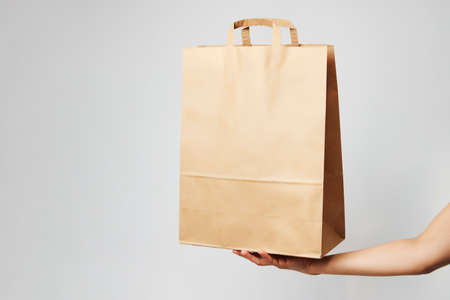 Woman holding brown paper bag on white background with copy space. Delivery and shipping service concept. Hand with paper shopping bag, close-up.の写真素材