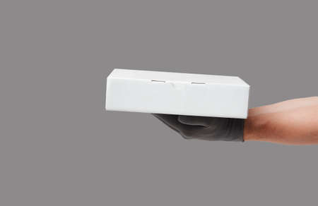Hand holding cardboard box on over grey background with copy space. Delivery and shipping service...