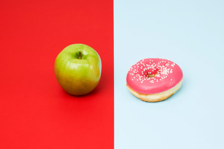 Green apple and red donut background. Weight loss concept. Healthy and junk food.の写真素材