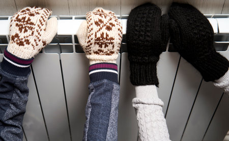 Woman warming her hands on the heater, close-up. Hands and heater radiator as cold winter conceptの写真素材