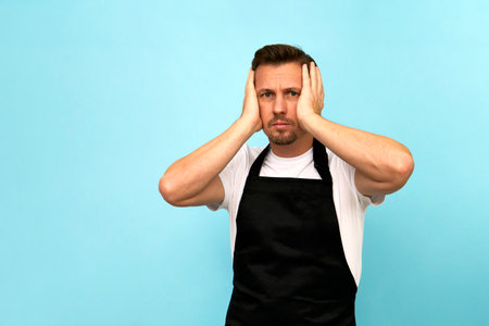 Young barista in black apron and white t-shirt on blue background with copy space. Man wearing chef apron, close-upの写真素材