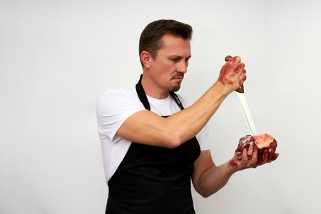 Young butcher in a black apron holding piece of meat and knife.