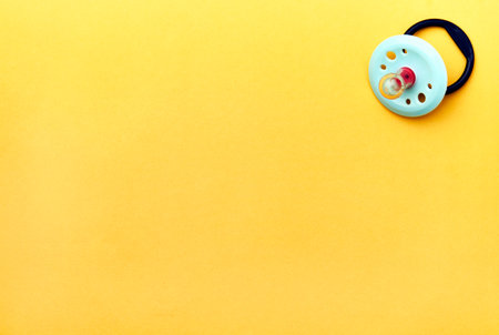 Baby pacifier on a yellow background with copy space. Rubber pacifier, top view