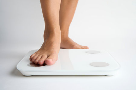 Woman legs stepping on floor scales, close-up. Female bare feet standing on scales, white background. Diet and overweight concept.の写真素材