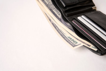 Black leather wallet with dollar money on a white background with copy space, close-upの写真素材