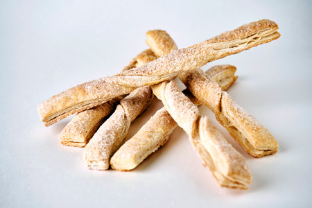 Puff pastry sticks with cinnamon on white background with copy space. Breadsticks sprinkled with...