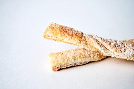 Puff pastry sticks with cinnamon on white background with copy space. Breadsticks sprinkled with sugar, close-upの写真素材