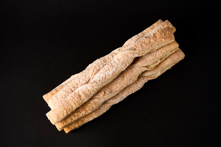 Puff pastry sticks with cinnamon on black background with copy space. Breadsticks sprinkled with...