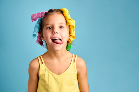 Little girl with curlers on blue background with copy space. Close-up portrait of a child girl with hair curlers, close-up. Kids beauty and fashionの写真素材