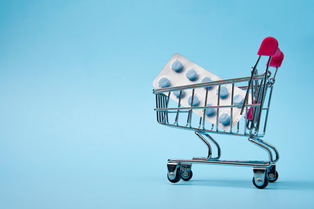 Shopping cart with medicines on blue background with copy space, close-up. Pharmaceutical deliveryの写真素材