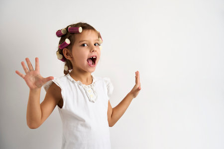 Little girl with curlers on white background with copy space. Close-up portrait of a child girl with hair curlers. Kids beauty and fashionの写真素材