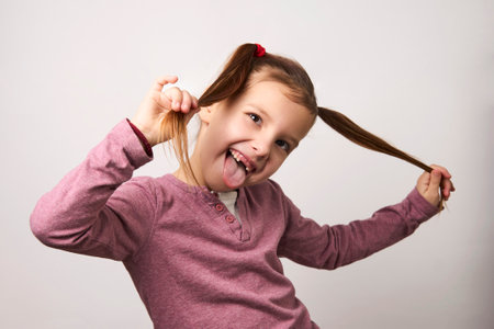 Portrait of a cute girl holding her hairs, close-up. Happy smiling child girl on white background with copy spaceの写真素材