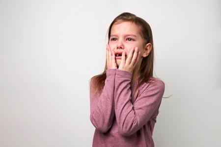 Crying child girl against white background with copy space. Portrait of a sad baby girl with tear drops on eyes, close-upの写真素材