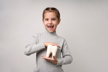 Little girl holding tooth on a white background with copy space. Portrait of happy girl with white...