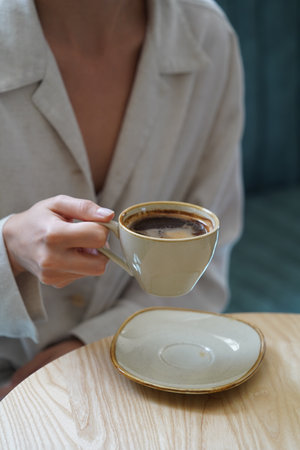 Woman hand holding coffee cup. Woman sitting at table and drinking coffee, close-upの写真素材