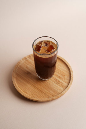Iced coffee glass on wooden tray, light background, close-up. Cold brew coffee drink with ice cubesの写真素材