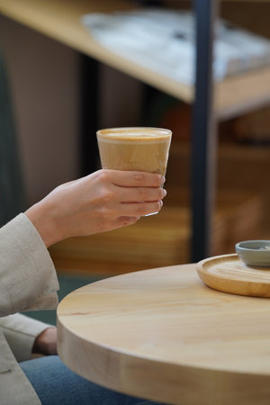 Woman hand holding coffee cup. Woman sitting at table and drinking coffee, close-upの写真素材