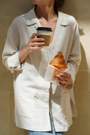 Young woman having breakfast at park, outdoor. Woman hand holding coffee and croissantの写真素材