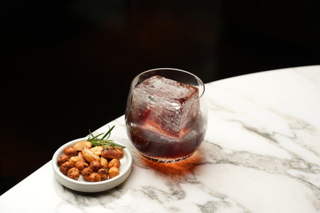 Whiskey cocktail glass and nuts snack on a marble bar counter. Alcohol cocktail drink, close-up....
