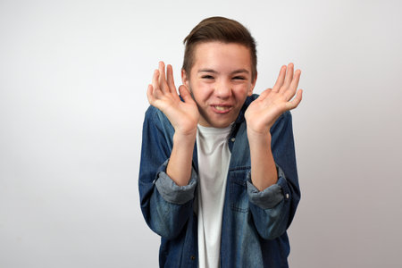 Surprised boy in casual clothes looking at camera with funny face and raised his hands up gesture, white backgroundの写真素材