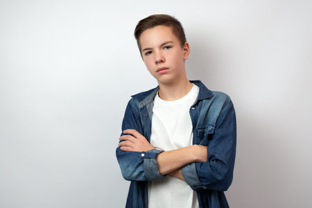Portrait of teenage boy with crossed arms, standing looking camera, white background with copy spaceの写真素材