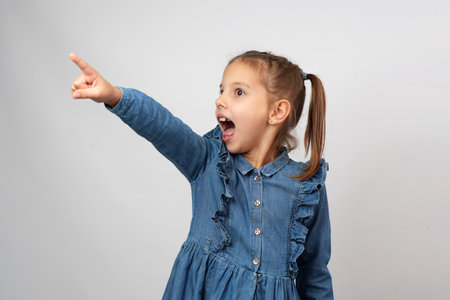 Cute happy girl pointing finger in copy space isolated on white backgroundの写真素材