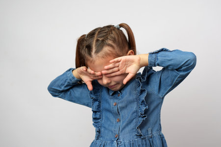 Cute little crying girl covering eyes with hand, white background with copy space. Childhood depressionの写真素材