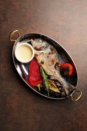 Fried fish with vegetable on frying pan on brown table backgroundの写真素材