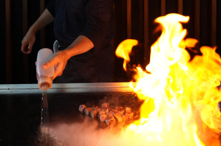 Chef cooking at stove with fire flame, close-up, selective focus. Chef cook food with fire at kitchen restaurantの写真素材