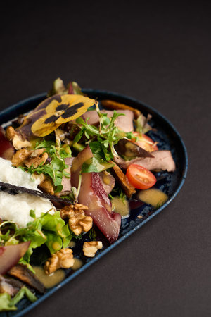 Healthy beef salad with vegetables and fruits. Boiled meat and walnuts, tomato, herbs and other ingredients on a black tray. Summer saladの写真素材