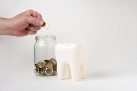 Hand put coin money in a glass jar and white tooth model, isolated on white background with copy space. Dental Insurance conceptの写真素材