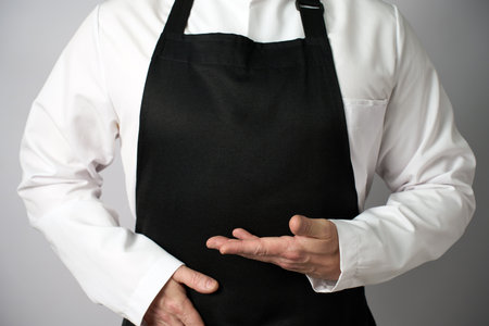Male chef wearing apron and pointing with hand, close-up, standing on a white background. Can be used for restaurant menuの写真素材